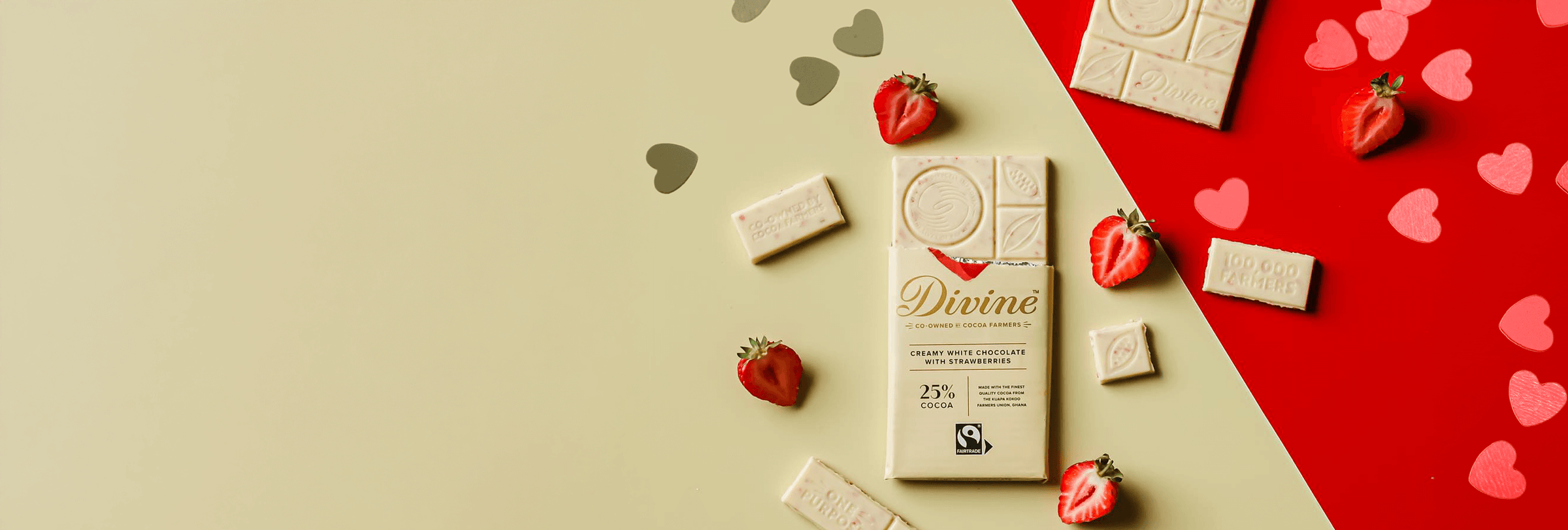 White chocolate bar with the label "Divine" surrounded by strawberries and chocolate pieces on a split beige and red background with heart shapes.