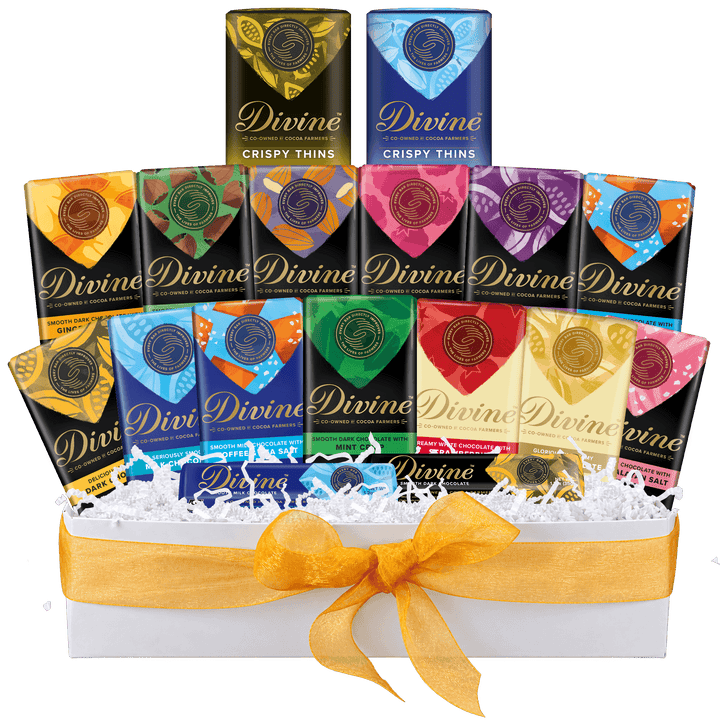 A Divine Crispy Thins chocolate gift set arranged in a white box with white shredded paper and a yellow ribbon. Multiple individually wrapped bars in assorted colors are visible behind the front row, including black, blue, orange, green, pink, red, and gold packages, all branded Divine.