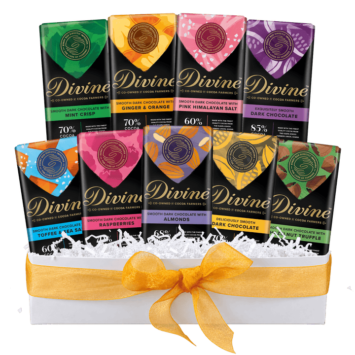 A Divine chocolate gift set in a white box filled with white shredded paper and tied with a yellow ribbon. The set includes multiple flavors of Divine chocolate bars, each with a colorful label and different cocoa percentages.